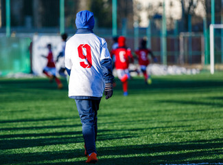 Boys in white red sportswear running on soccer field with snow on background. Young footballers dribble and kick football ball in game. Training, active lifestyle, sport, children winter activity 