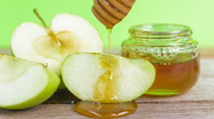 Jewish holiday, Apple Rosh Hashanah, on the photo have honey in jar and drop honey on green apples on wooden with green background