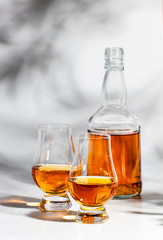 Scotch Whiskey without ice in glasses and bottle, white background with hard light, shadows and sun glare, copy space