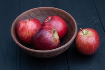 Red apples in a clay cup on a dark wooden background.