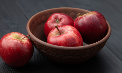 Red apples in a clay cup on a dark wooden background.
