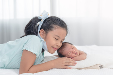 Obraz na płótnie Canvas Sister happy welcome her little brother. Toddler kid meeting new sibling. Cute girl and new born baby boy relax in a white bedroom. Family with children at home.