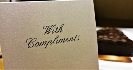 A With Compliments note in a hotel room with a slice of chocolate cake in the background