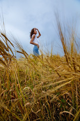 Selective focus. Wheat ears against the silhouette of a girl standing in the middle of a field and a cloudy sky.
