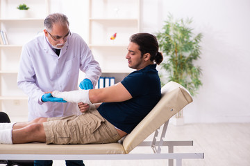 Obraz premium Young injured man visiting old doctor traumatologist