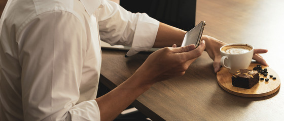 businessman using smartphone to take a photo of coffee and brownie before eating breakfast in the...