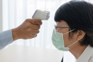 doctor using infrared digital thermometer to measure temperature of senior asian woman patient that was sick and came visit at the clinic in hospital. healthcare and medical concept