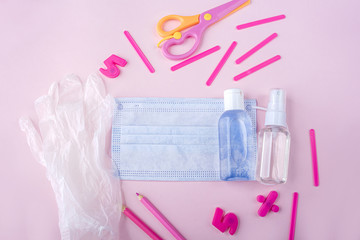 Education or back to school concept. Set of blue school supplies, medical face mask and antiseptic sanitizer gel on pink. New normal during coronavirus pandemic. Virus protection, keep distance