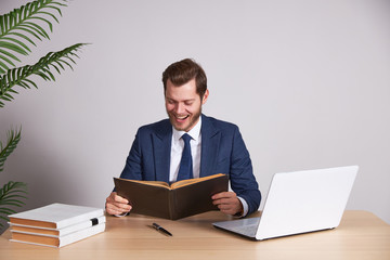 A businessman in a blue business suit holds a book and smiles. White background. Looks into the book.