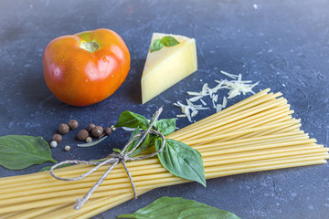 Fresh ingredients for cocking pasta with Traditiona Italian sauce Pesto. Dry Spaghetti, Basil leaves, tomato, parmesan on dark background. Copy sapce for text