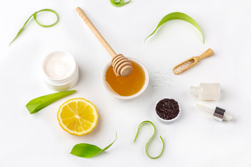 Natural organic ingredients homemade skin care. Cleansing and nourishing cosmetic. Beauty products: cream, honey, coffee scrub,  among green leaves on white background. Close up, copy space for text