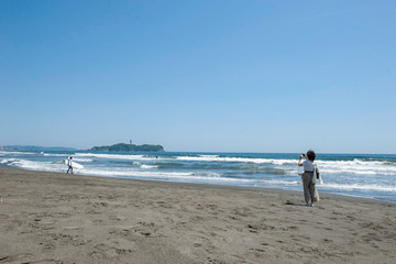 湘南　鵠沼海岸と江ノ島と浜辺でスマホで写真を撮影する若い女性