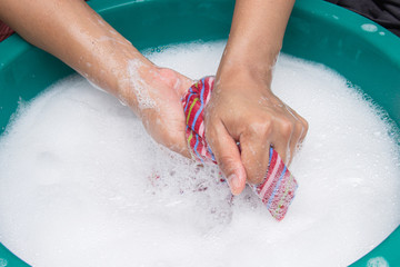 Fototapeta premium Female hands wash clothing by hand with detergent in basin. selective focus and space for text.
