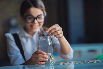 Dark-haired girl putting coins into the jar and smiling