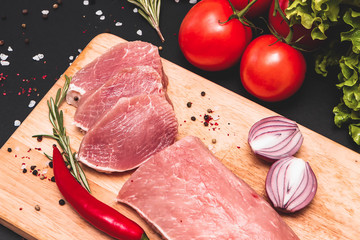 Raw juicy meat steaks ready for roasting on a black chalk board background. fillet with cherry tomatoes, hot pepper and herbs.