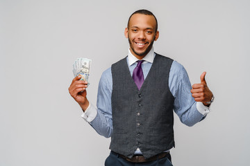 Portrait of excited young african american man holding cash money and showing thumb up over light grey background