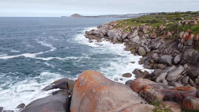 A drone flight above the surrounding rocks with waves breaking around Granite Island Victor Harbor South Australia