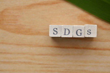 The word cube formed "SDGs" with a green grass on wooden board.