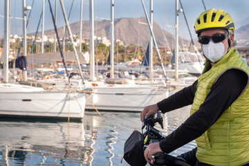 Senior man with helmet enjoying excursion at sea with his bicycle wearing surgical mask due to...