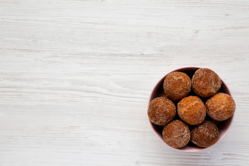 Homemade Fried Donut Holes in a pink bowl on a white wooden background, top view. Flat lay, overhead, from above. Copy space.