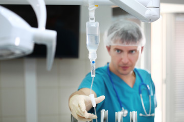 The doctor checks the IV. The man is out of focus. Photo in the operating room. Copy of the space. - obrazy, fototapety, plakaty