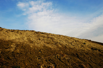 The slope of a clay hill against the backdrop of a beautiful blue sky. Lifeless soil. Sunny...