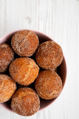 Homemade Fried Donut Holes in a pink bowl on a white wooden background, side view.