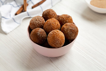 Homemade Fried Donut Holes in a pink bowl on a white wooden background, side view.