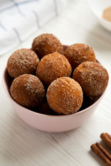 Homemade Fried Donut Holes in a pink bowl on a white wooden surface, side view.