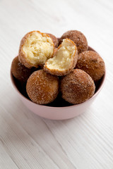 Homemade Fried Donut Holes in a pink bowl on a white wooden background, side view.