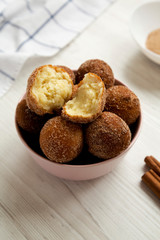 Homemade Fried Donut Holes in a pink bowl on a white wooden surface, side view.