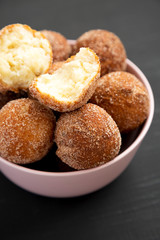 Homemade Fried Donut Holes in a pink bowl on a black background, side view.