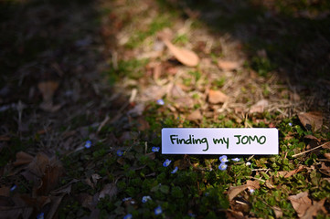 The letters "Finding my JOMO" printed on a piece of paper in wild ground.