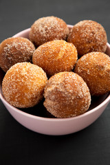 Homemade Fried Donut Holes in a pink bowl on a black background, low angle view. Close-up.
