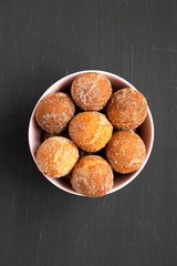 Homemade Fried Donut Holes in a pink bowl on a black background, top view. Flat lay, overhead, from above.