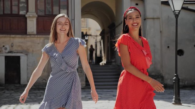 Two best cheerful friends holding hands, laughing, walking and dancing on a background of the old city.