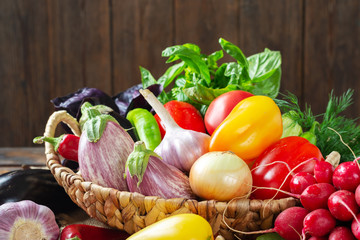 Assortment of vegetables in a basket on the table. A lot of different raw vegetables in the basket. Eggplant, tomatoes, garlic, sweet pepper, onion on the table. The concept of healthy eating