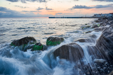 Long exposure of the coastal landscape of Imereti Adler beach with warm evening light, when the waves wash over rocks covered with seaweed