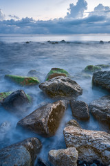 Long exposure of the coastal landscape of Imereti Adler beach with warm evening light, when the waves wash over rocks covered with seaweed