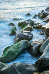 Long exposure of the coastal landscape of Imereti Adler beach with warm evening light, when the waves wash over rocks covered with seaweed