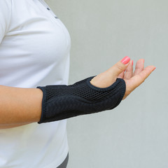 Black wrist brace or corset is worn on women's hand for treatment of carpal tunnel syndrome or...