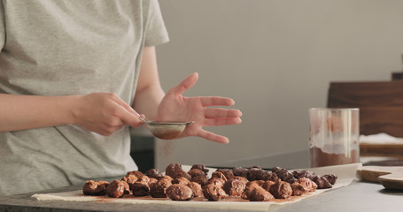 young woman sprinkle cocoa powder on chocolate truffles