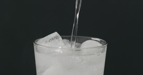 pour soda in glass with ice cubes on black background closeup