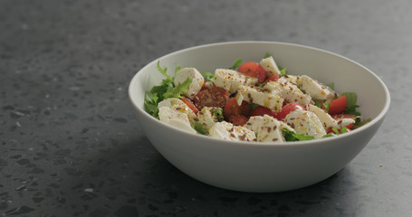 salad with mozzarella, cherry tomatoes and frisee leaves in white bowl on terrazzo surface