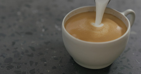 pouring steamed milk into cappuccino in white cup on terrazzo countertop