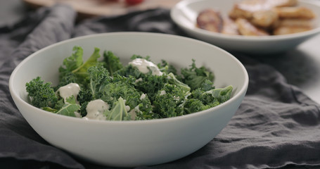 pour caesar dressing on kale leaves in white bowl