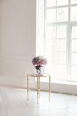 Cozy home decor. A bouquet of hydrangeas in glass vase by window on coffee table. A bouquet of flowers on a table in white room at home. Classic living room interior. Scandinavian interior.