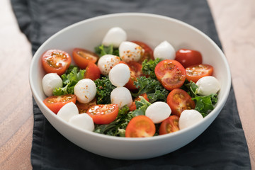 Salad with kale, tomatoes and mozzarella in white bowl