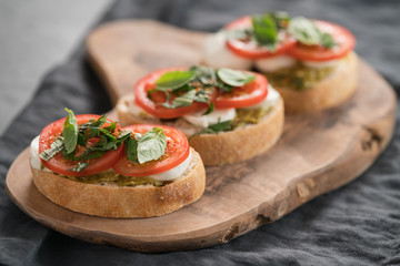 Bruschetta with mozzarella, tomatoes and basil with pesto on olive wood board