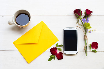 mobile phone ,hot coffee espresso ,yellow envelope and red rose arrangement flat lay style on background white wooden